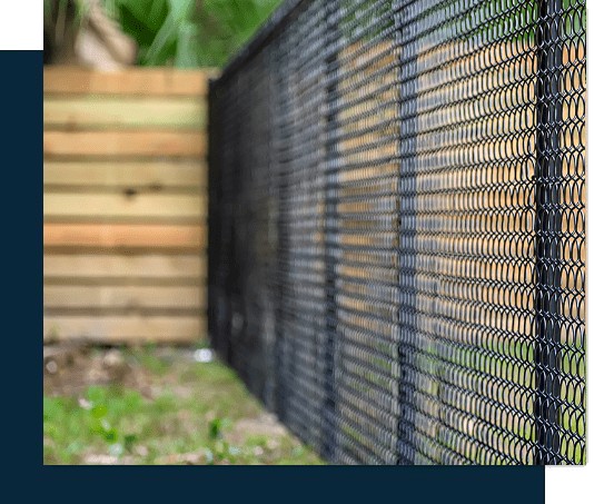 Side view of a black chain-link fence next to a wooden one, crafted by a skilled fencing installer in Central PA, with grass and blurred greenery in the background.