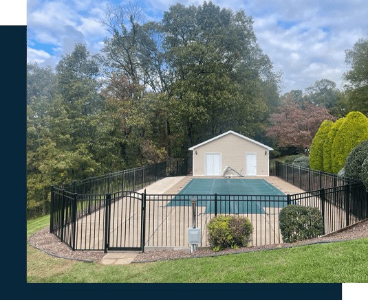 A fenced-in area, crafted by a skilled fencing installer in Central PA, encloses a covered pool and a cozy building. This tranquil space is embraced by lush trees and shrubs under a partly cloudy sky.