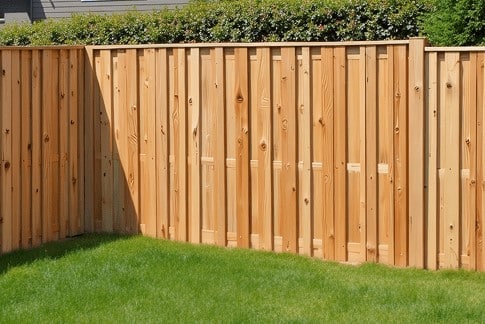 A beautifully crafted wooden privacy fence with vertical planks encloses a lush grassy yard, where trees peek through the background—a testament to the skill of a fencing installer in Central PA.